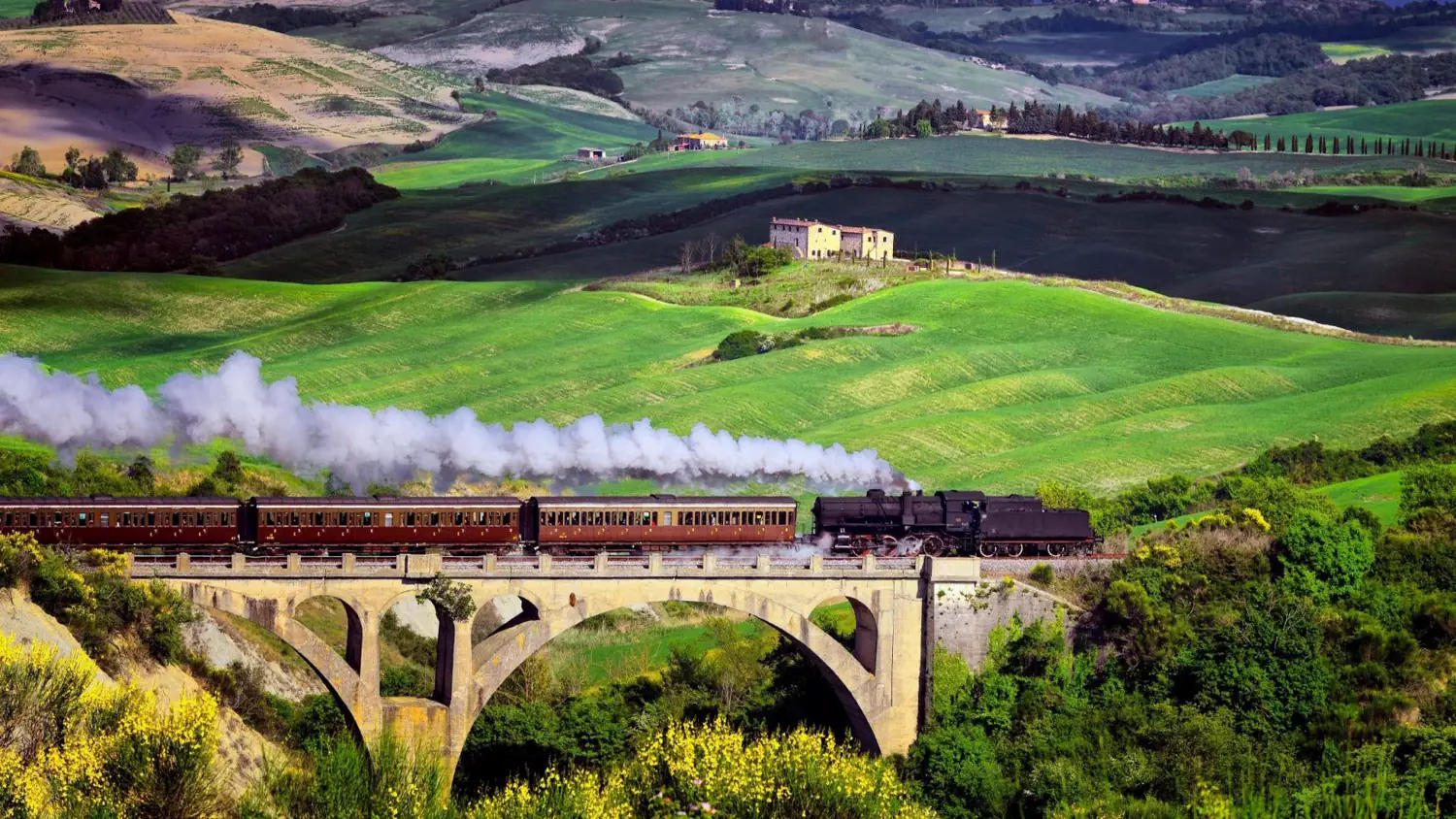 A vintage train crossing a viaduct through the Tuscan hills
