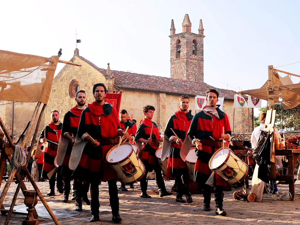 Medieval drummers in red and green processing through Monteriggioni